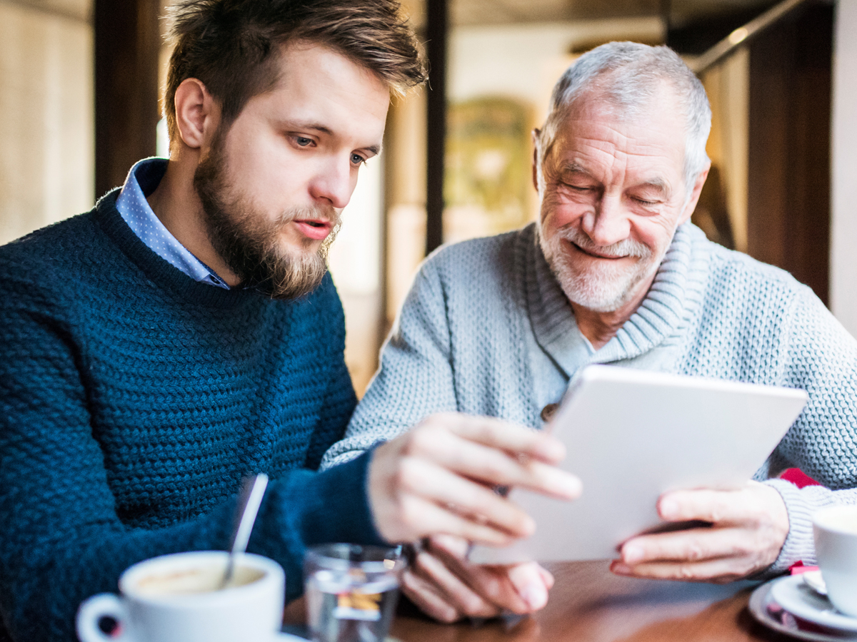 younger man helps older adult with technology