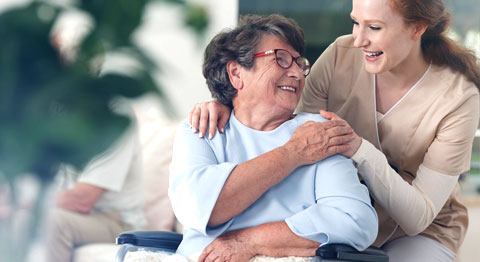 Elderly woman in a wheelchair and nurse smiling.
