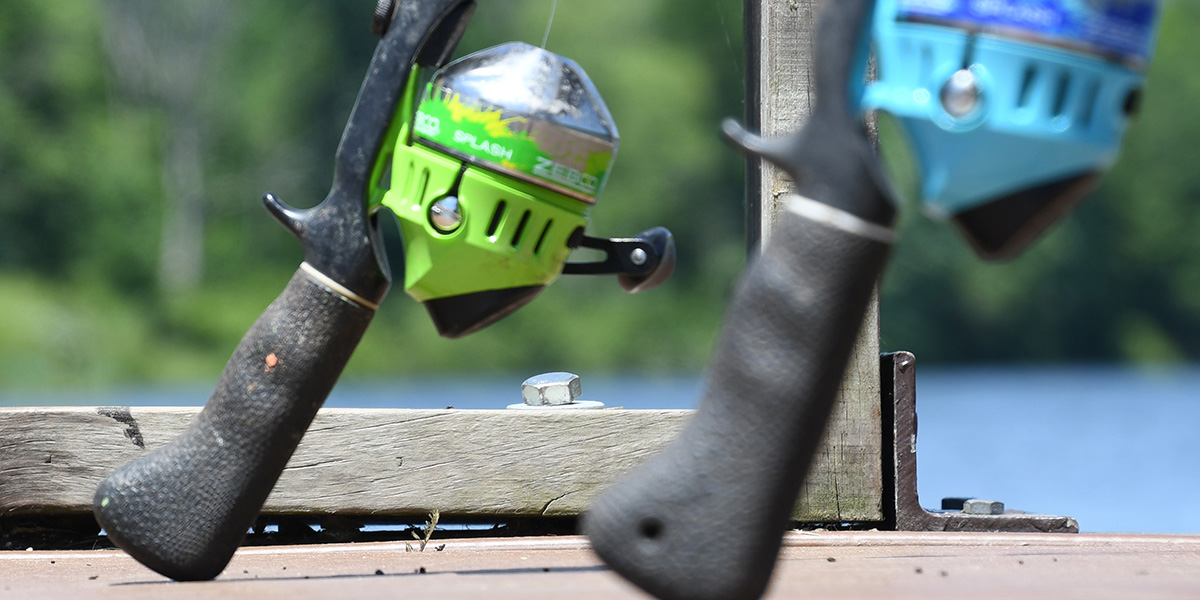 Close-up of two rods with closed-face reels leaning up against the railing of a wood dock.
