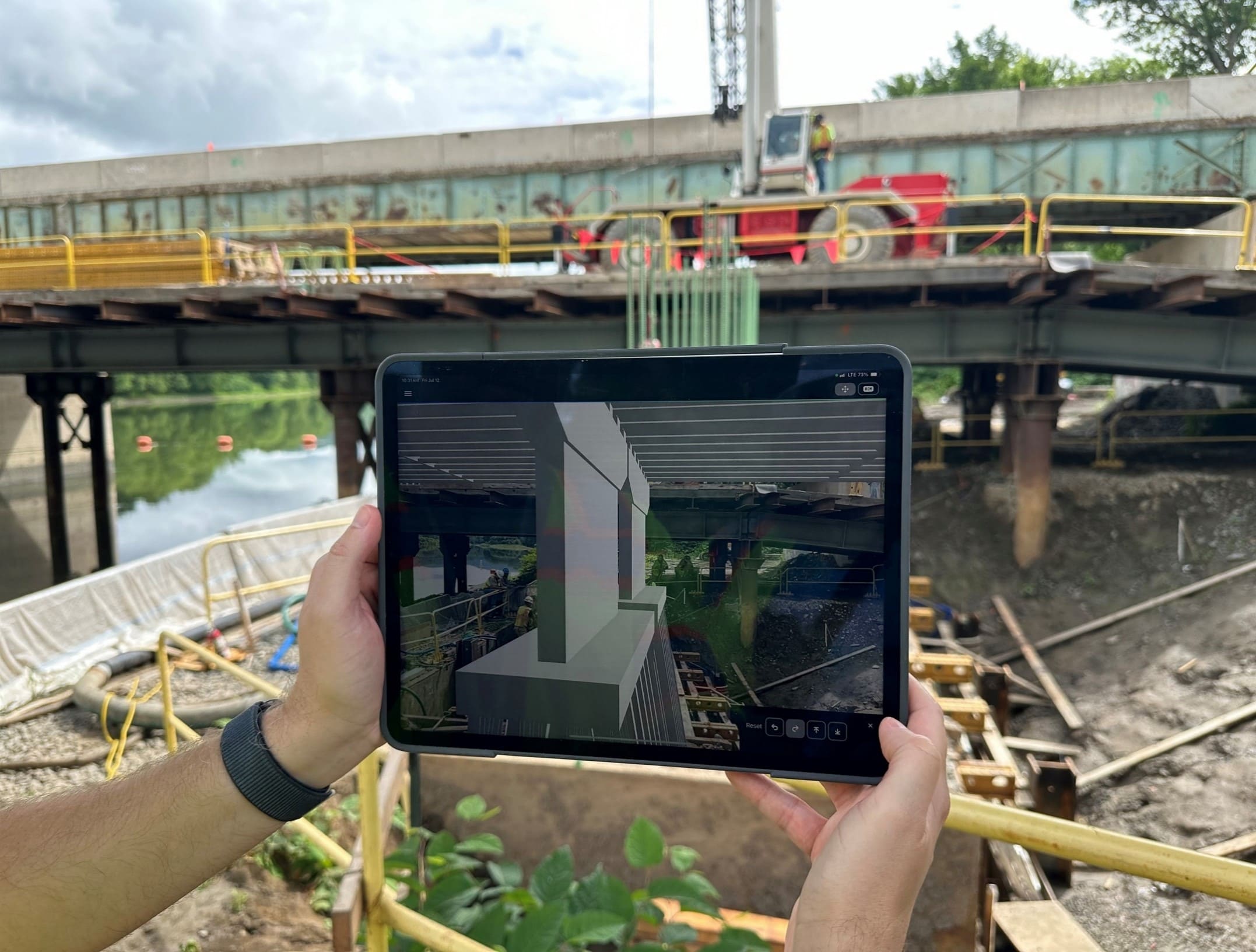 A photo of two hands holding a tablet taking images at a bridge construction site.