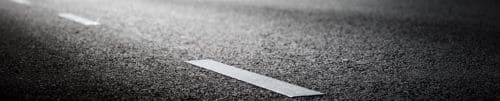 A close-up image of a roadway with a dotted white line. 