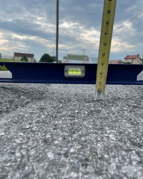 A close-up image of a metal level sitting on a roadway with a measuring tape up against it to show the trough that's developed on the roadway. 