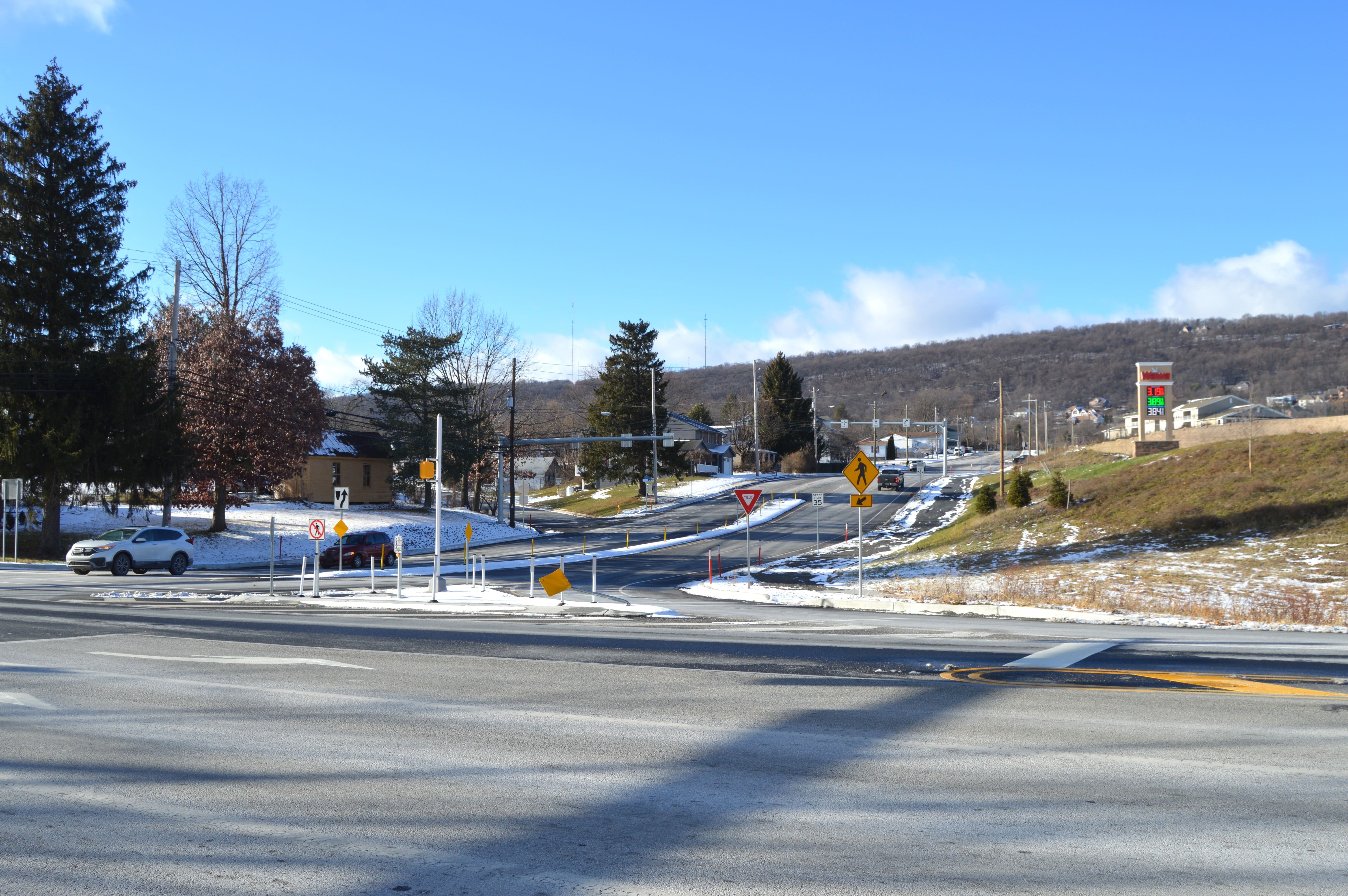 An image of a white SUV and red SUV entering an intersection to turn onto a four-lane roadway. Trees and houses sit on one side of the roadway and a convenience story sits on the other side.