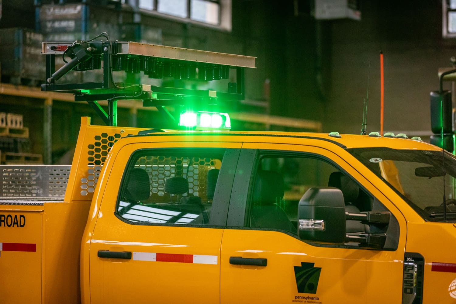 A green light flashes on top of a yellow PennDOT foreman crew cab sitting inside a maintenance garage. 