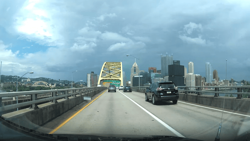 An image taken from inside a vehicle that's about to cross over a yellow steel bridge heading into the City of Pittsburgh. 