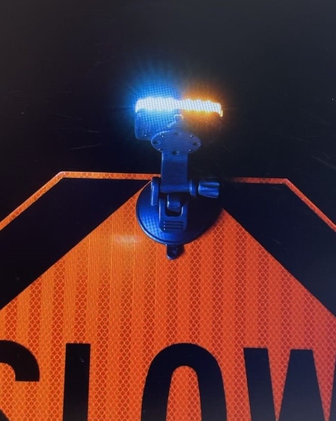 An image of an orange and black slow paddle sign used in a work zone with a reflective light attached to the top of it.