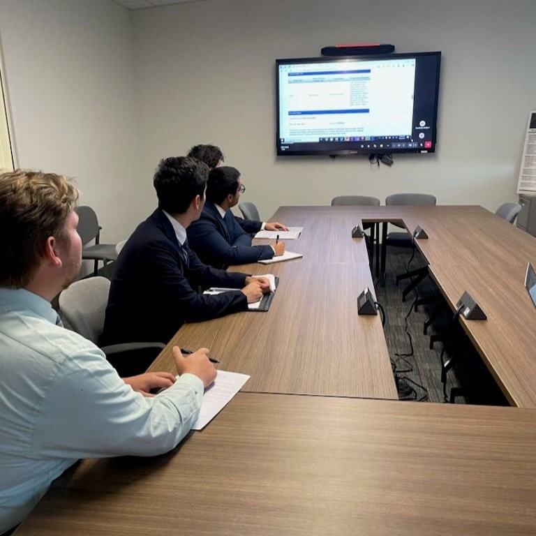 Four young men seated around a conference table participatingin a virtual meeting.