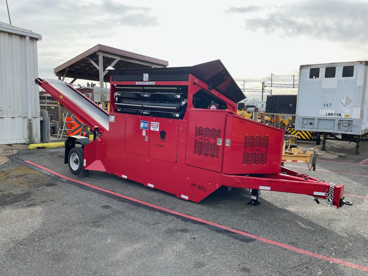 A large red piece of equipment mounted on a trailer chassis with a conveyor belt on one end and the trailer hookup on the other end. 