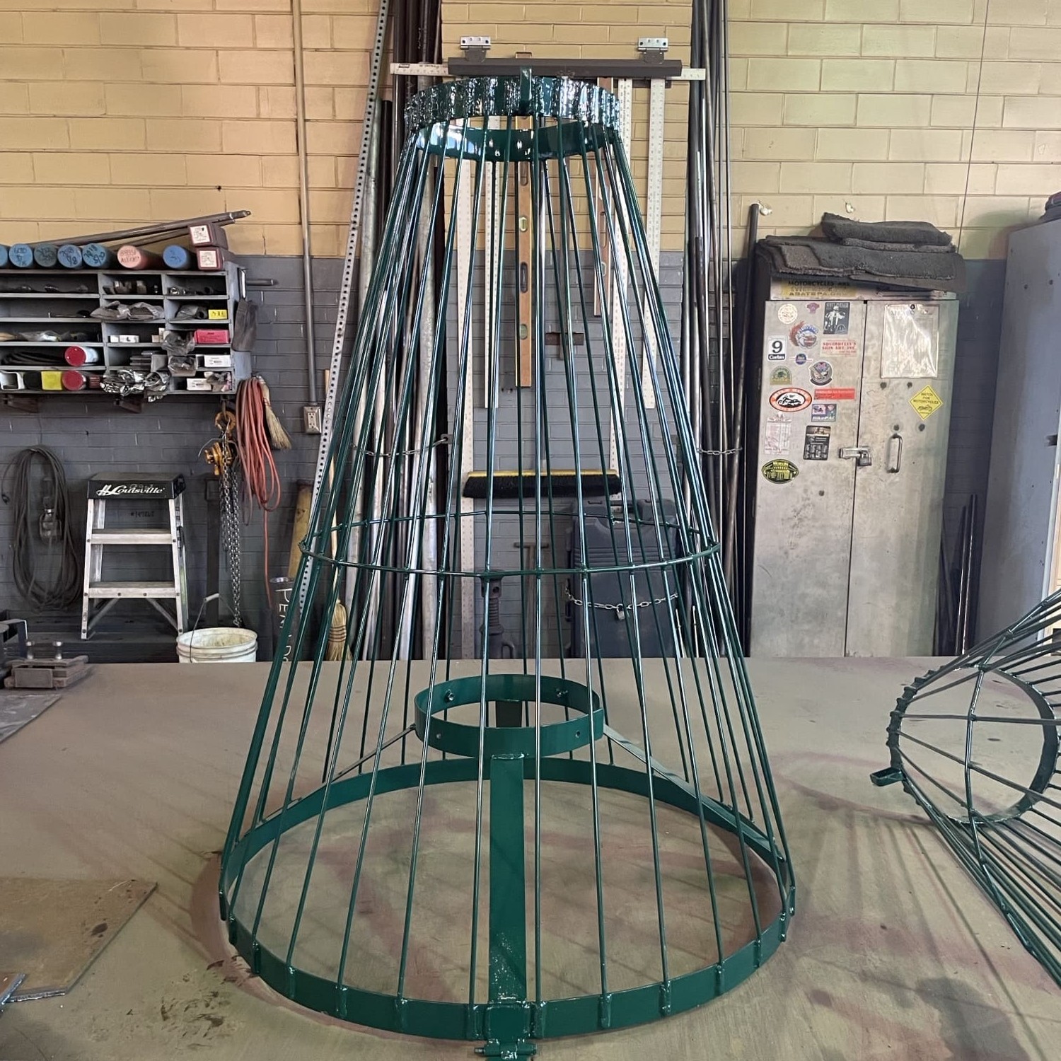 A green cylindrical cage stand vertically on a table in a maintenance shop.