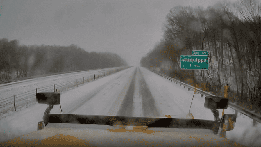 The front of a PennDOT plow truck from the operator’s perspective looking out at a snow-covered roadway.