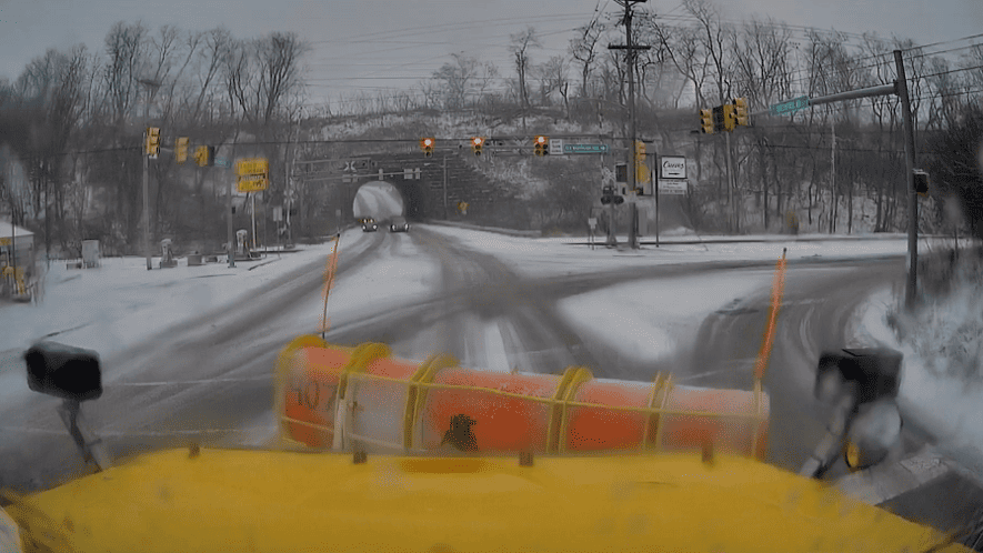 The front of a PennDOT plow truck from the operator's perspective looking out at a snow-covered roadway.