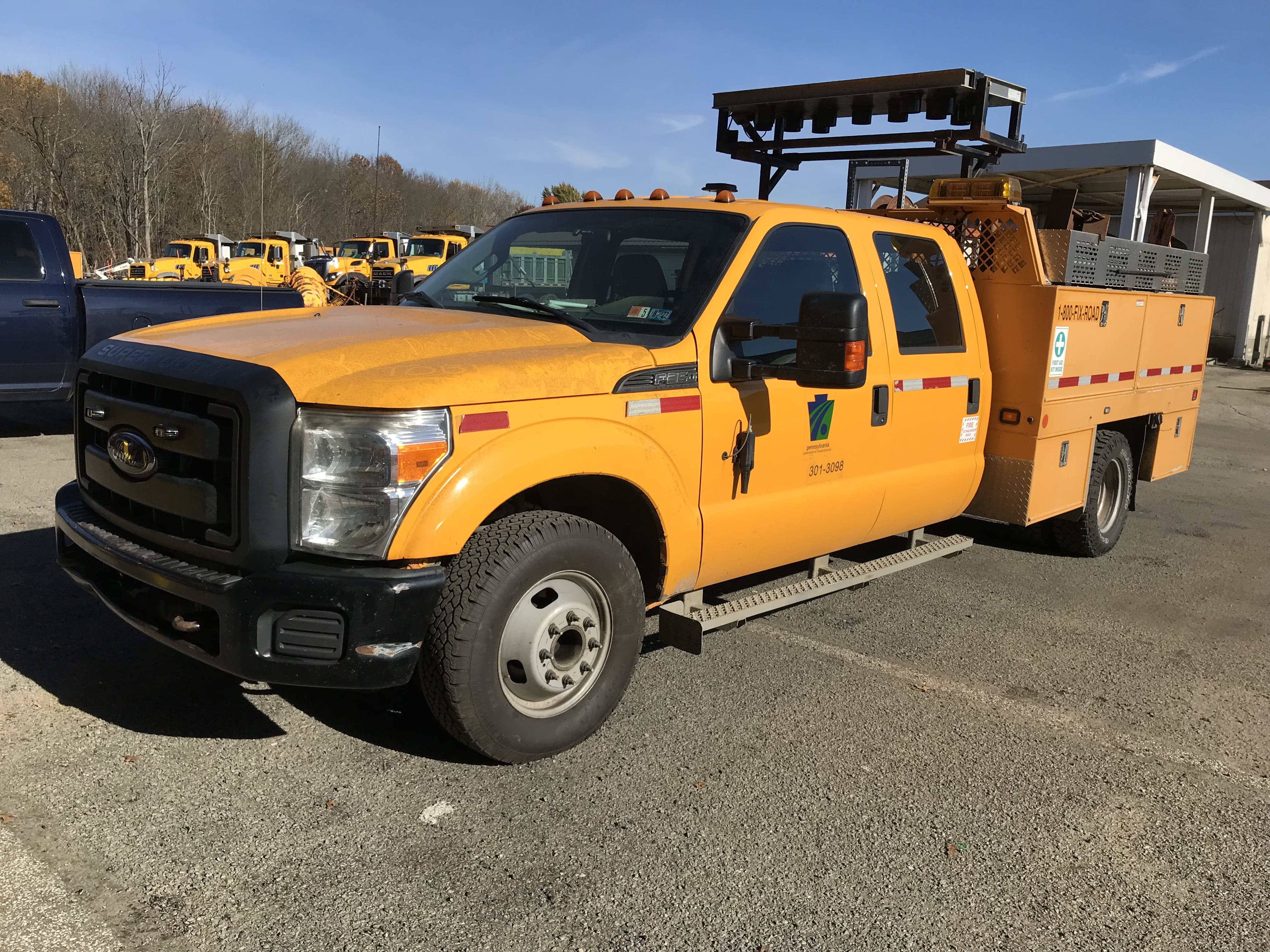 A yellow, four-door, crew cab truck sits in a parking lot. Trees and blue sky are in the background of the photo. 