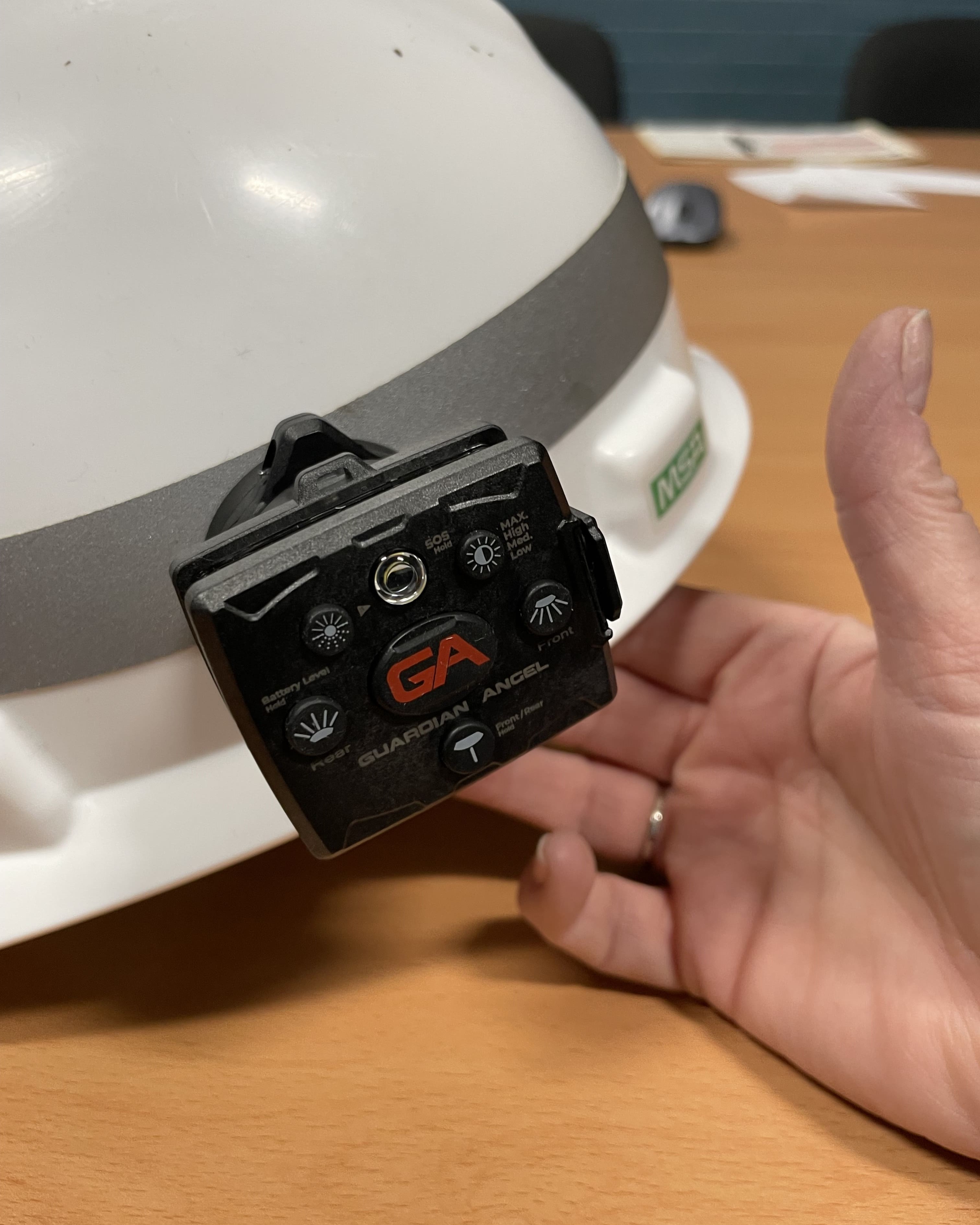 An image of a hand holding up a white hard hat with a reflective light affixed to the left side.