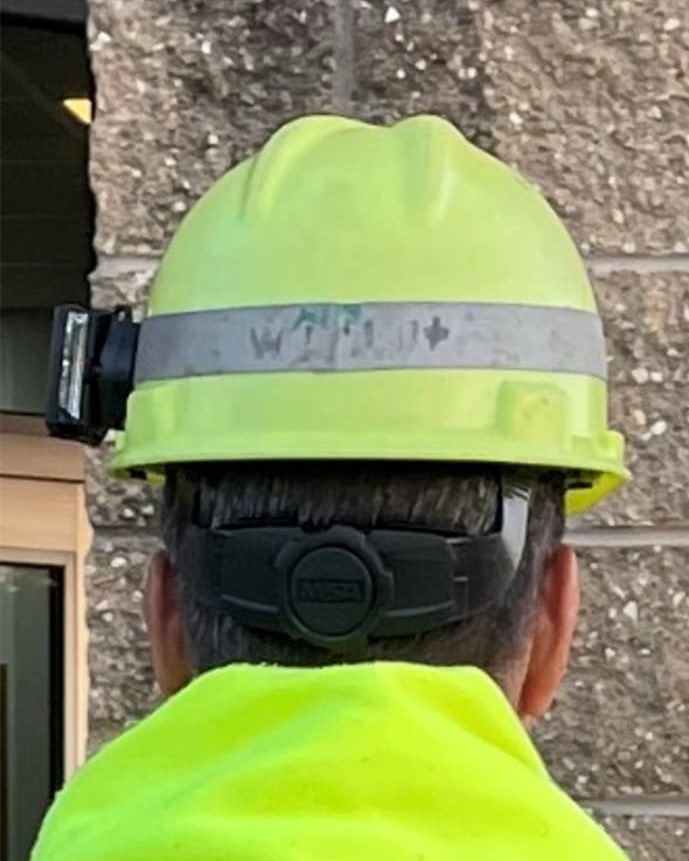 An image of the back of an individual’s head with a reflective light affixed on the left side of the individual’s yellow hard hat. 