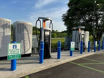 A row of electric vehicle charging stations sit along several parking spaces in a parking lot. 