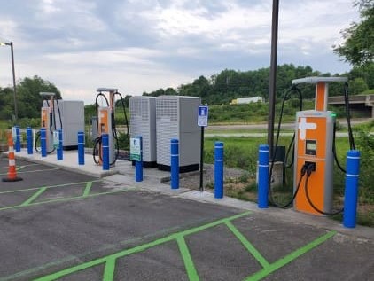 A row of electric vehicle charging stations sit along several parking spaces in a parking lot.