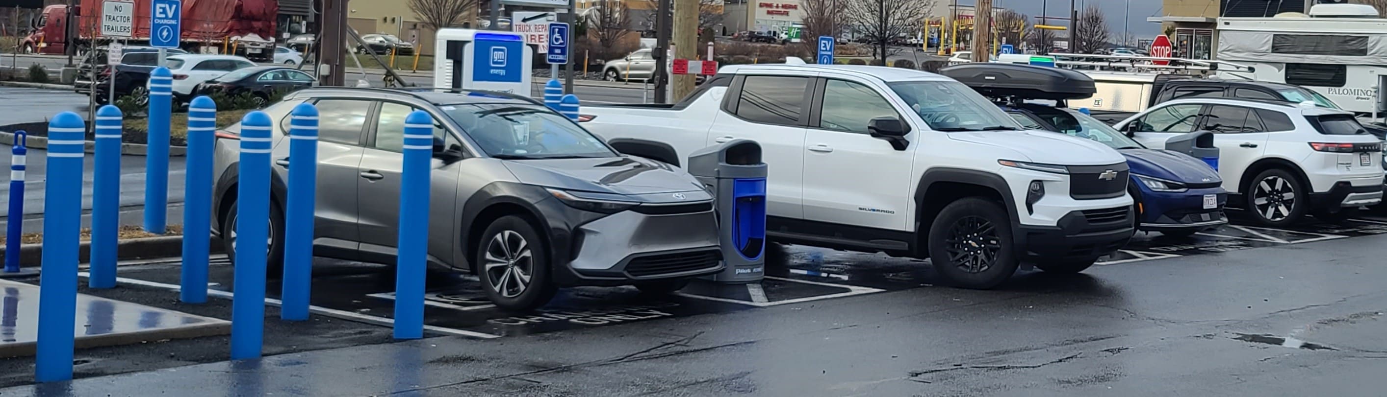 A line of cars sit in a parking lot next to electric vehicle charging stations. 