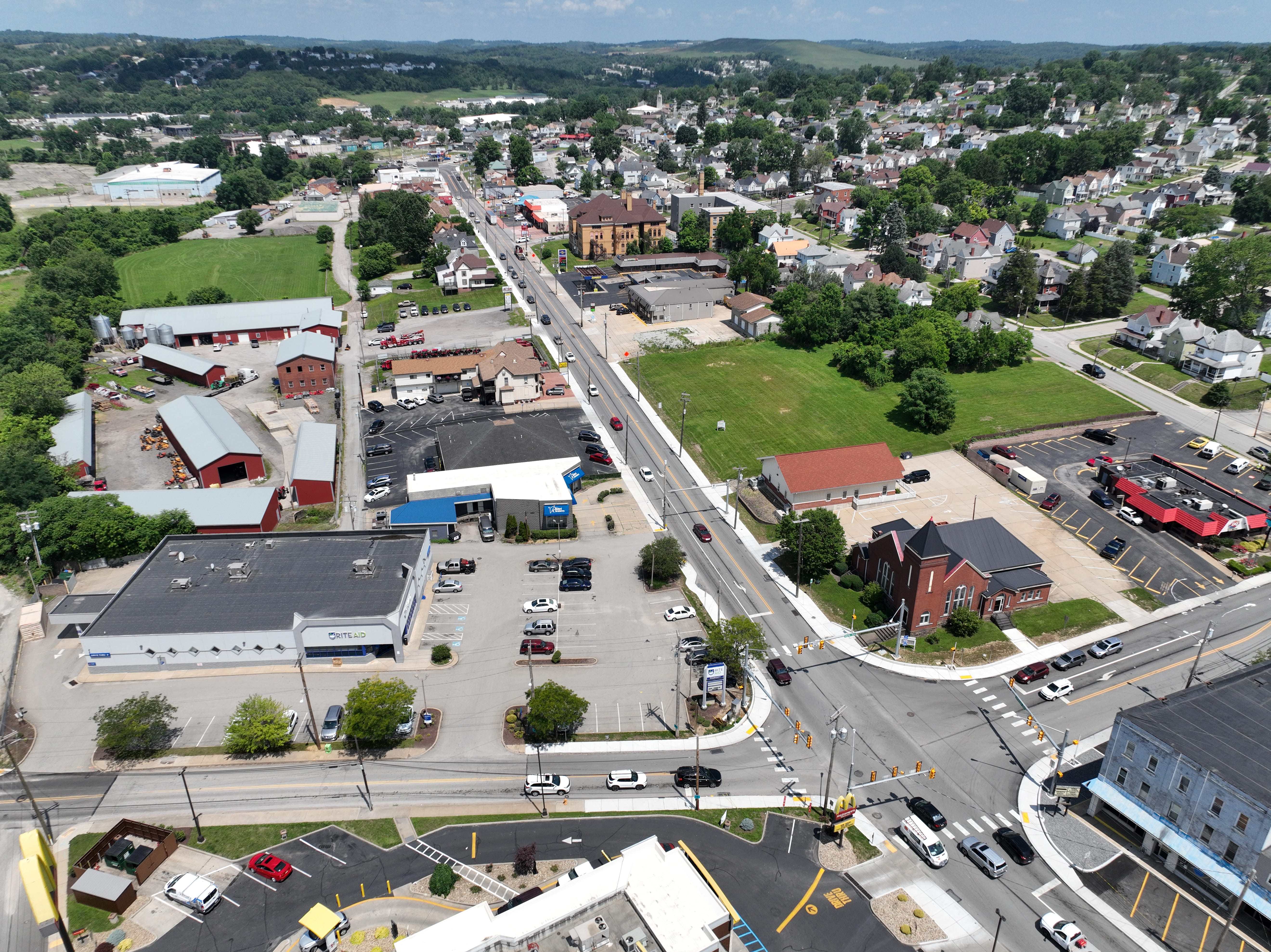 An aerial image of traffic navigating an intersection with traffic lights overhead. A brick church and multiple business surround the intersection. 