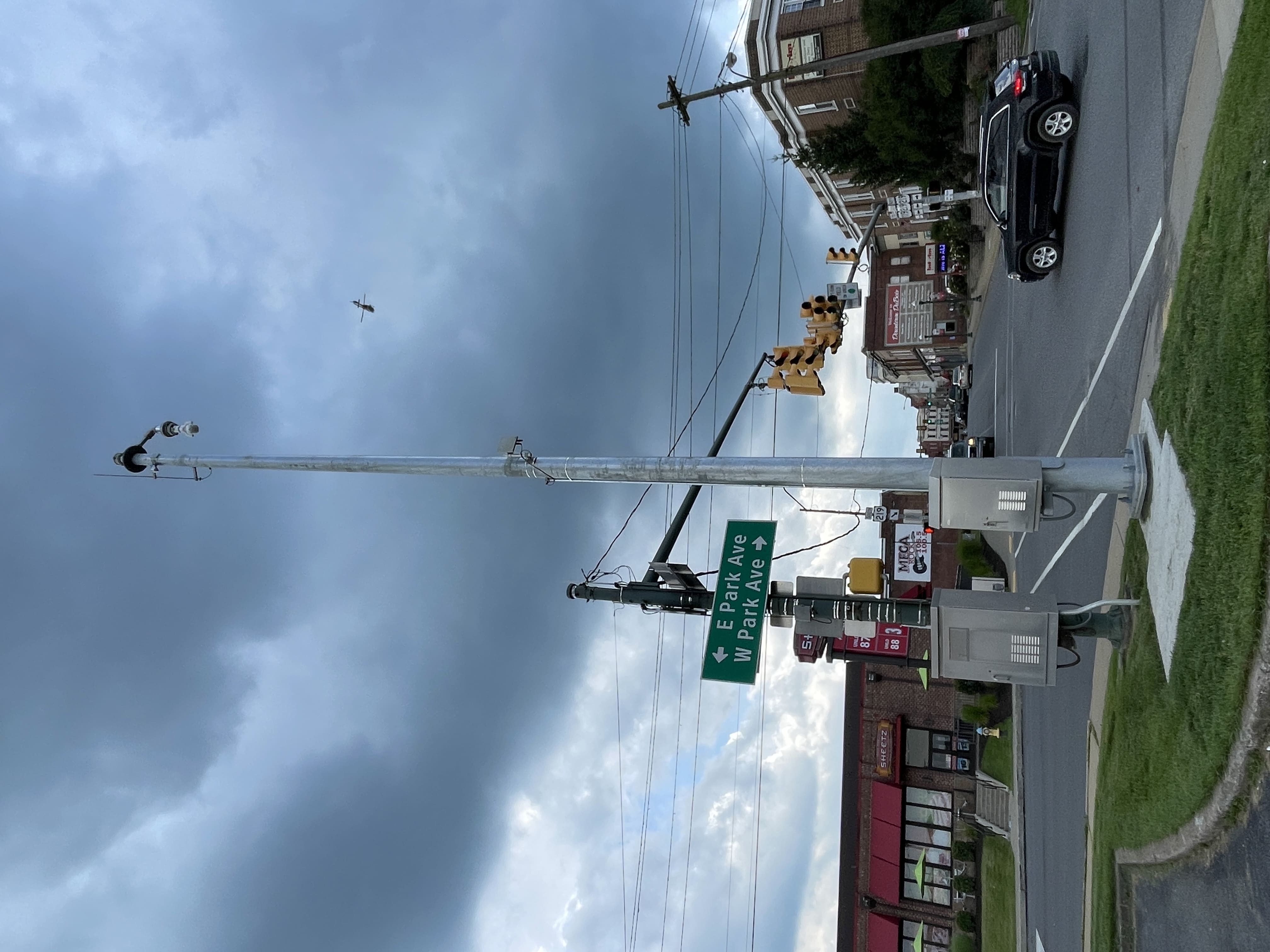 A black sports utility vehicle turns left at an intersection with traffic lights hanging overhead and a convenience store across the street.