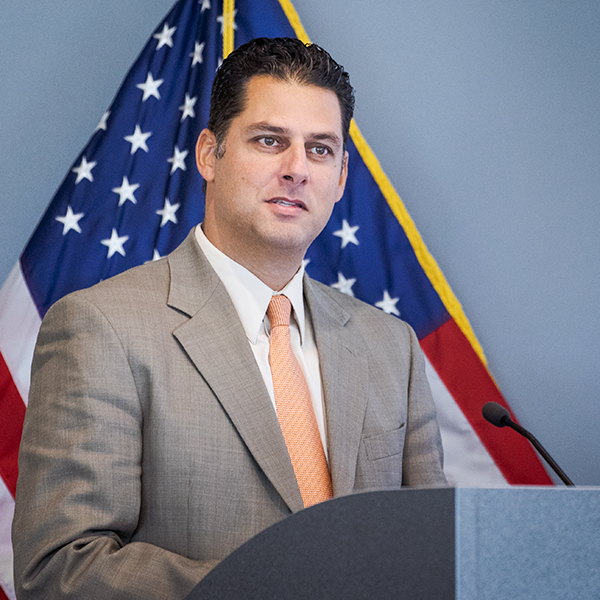 Gavin Gray speaking at a podium, American flag in background.