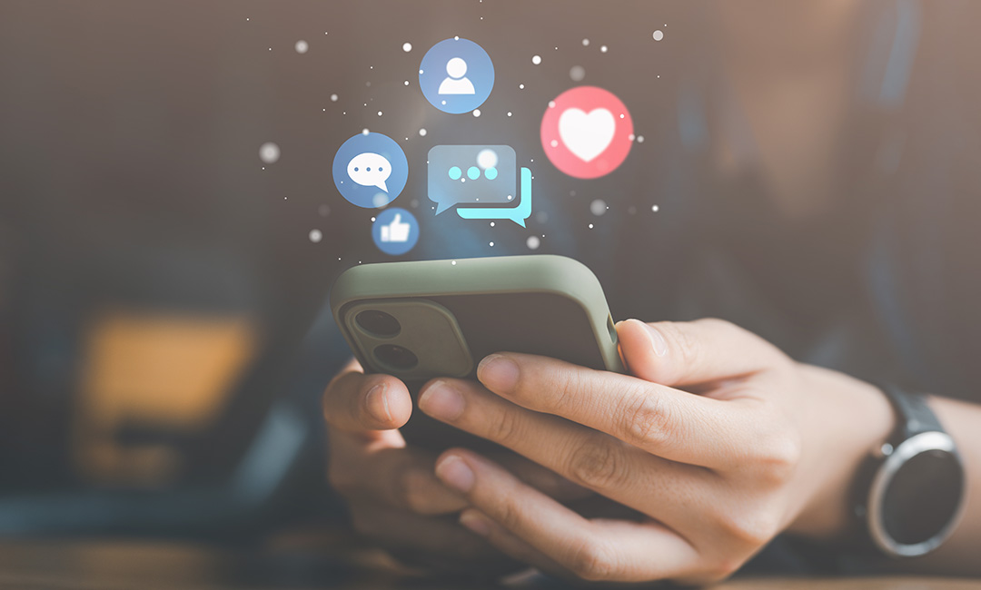 Hand holding a phone with social media icons above. 