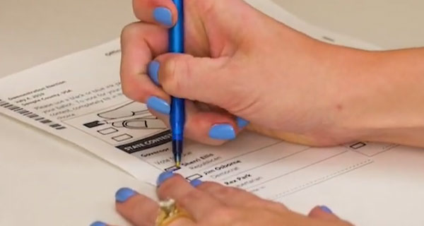 Person filling out a ballot with a pen